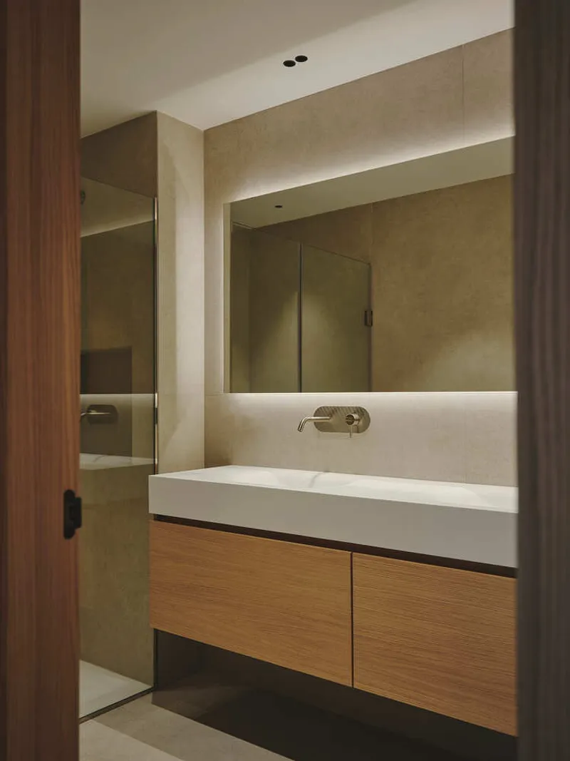 Bathroom vanity with oak cabinetry and backlit mirror under cove lighting