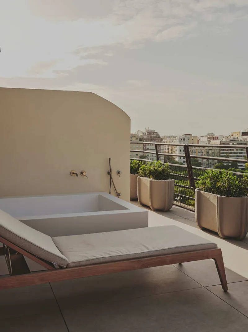 Rooftop terrace with sunken tub, curved stucco wall, and metal planters facing the city skyline