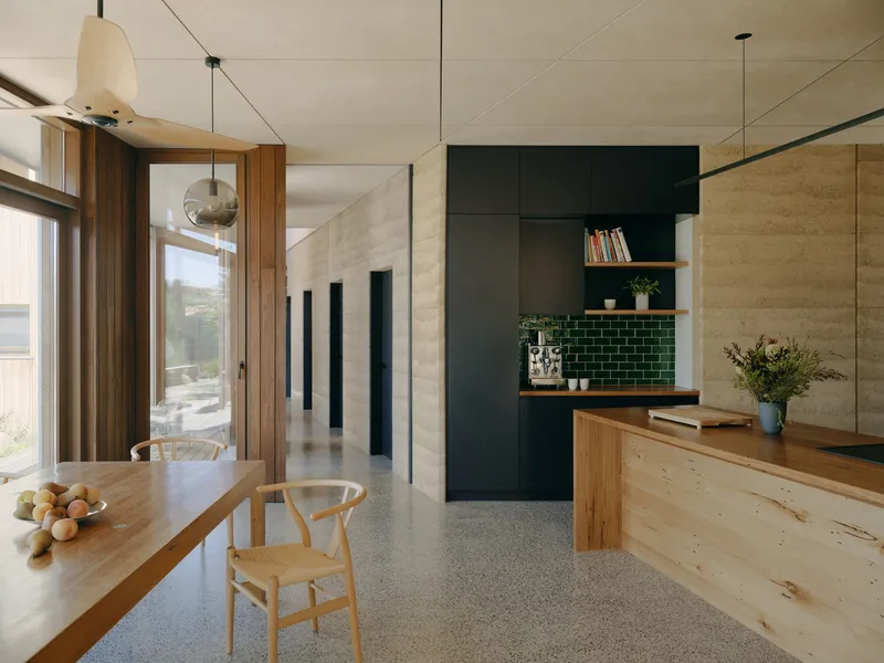 Open-plan kitchen and dining space with plywood ceiling, dark green tile backsplash and polished concrete floor