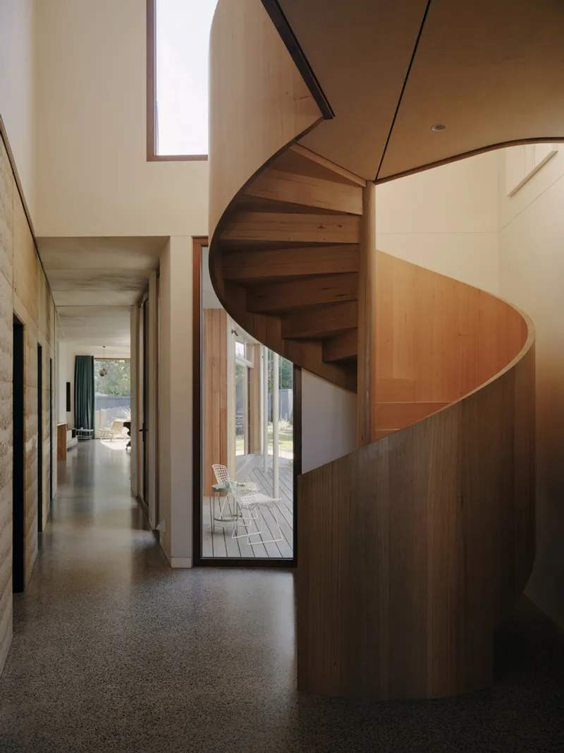 Curved timber staircase wrapping around plywood walls in the hallway with skylight above