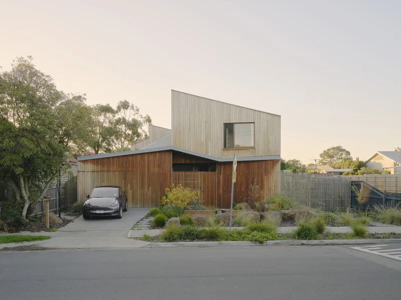 Front facade with two-story corrugated metal volume above horizontal timber cladding and planted rockery