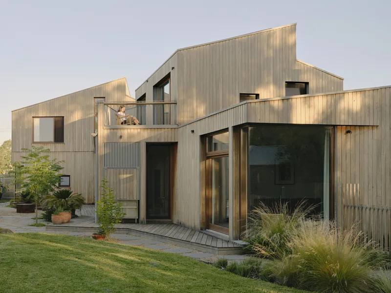 Garden elevation showing corrugated metal cladding with balconies and sliding glass doors at dusk