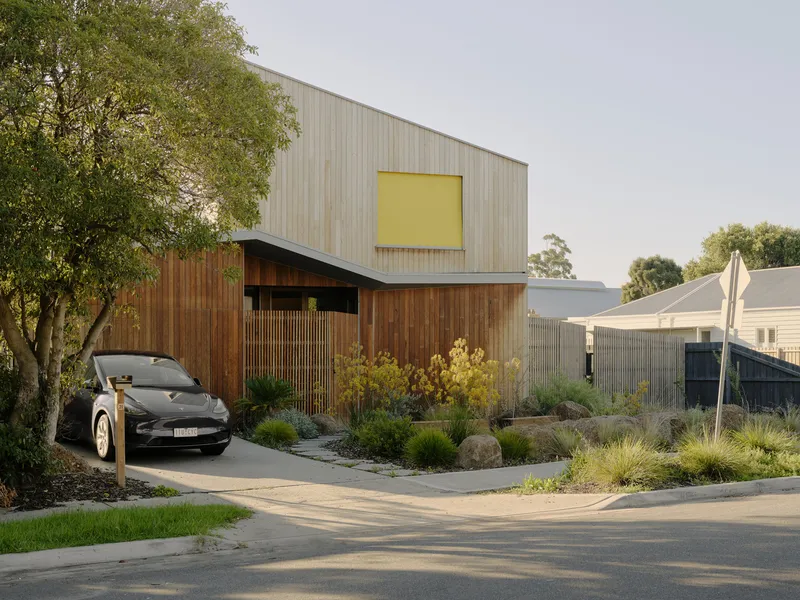 Front facade showing the yellow-paneled upper window and vertical timber slats at the carport entry