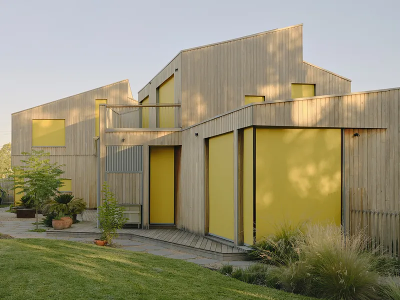 Rear elevation with yellow-glazed openings and terrace deck facing the lawn at dusk