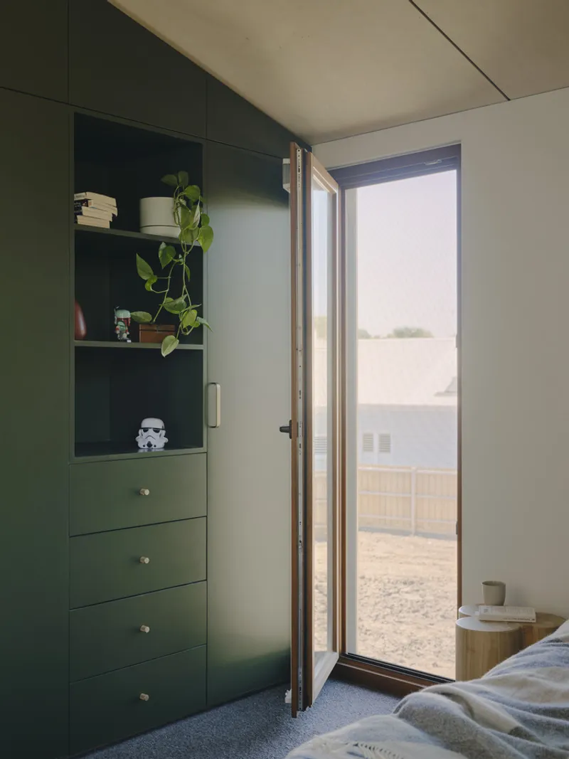 Bedroom corner with green built-in shelving and tall door opening to gravel courtyard