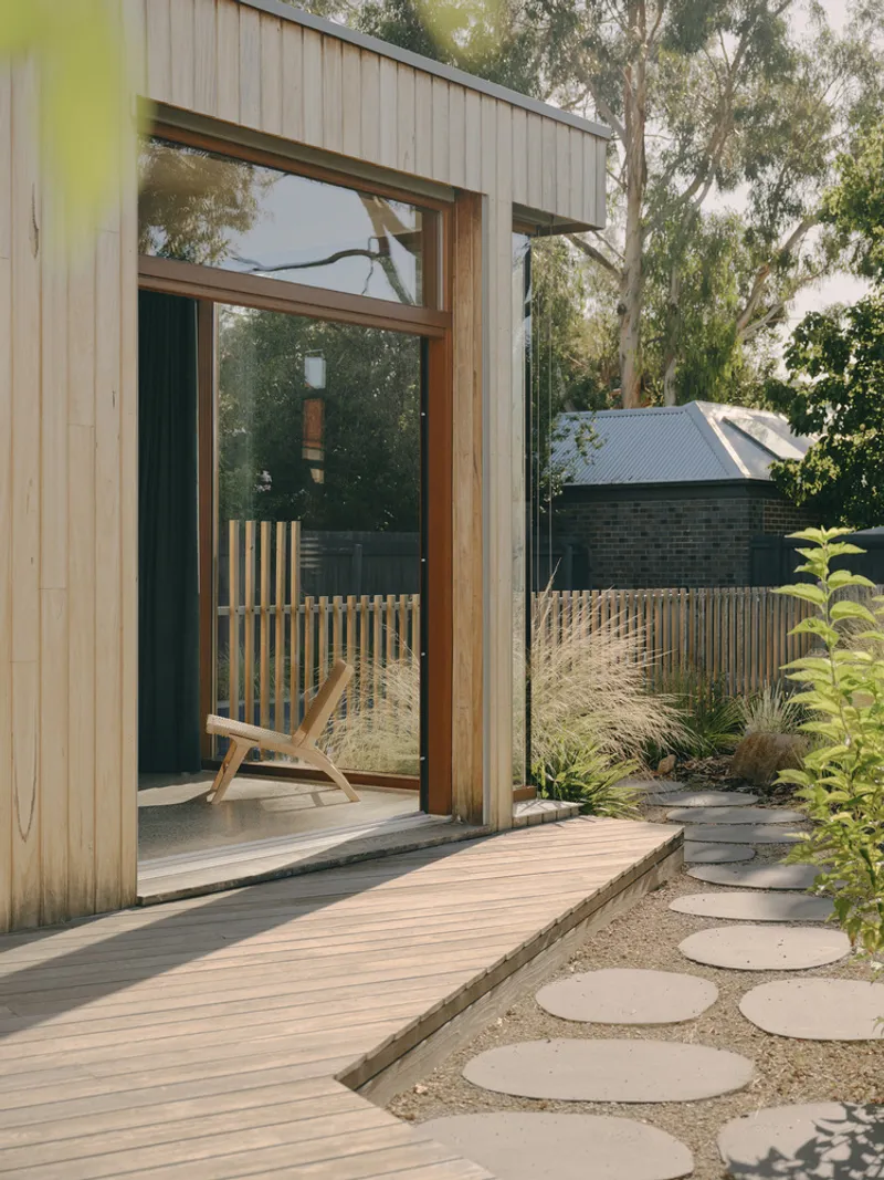 Timber deck and circular stepping stones leading to glazed door under eucalyptus trees