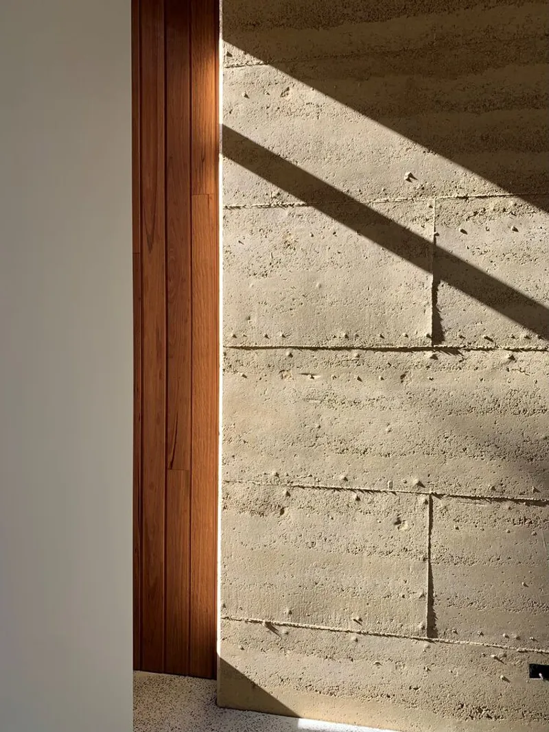Timber door frame meeting rammed earth block wall in afternoon sunlight