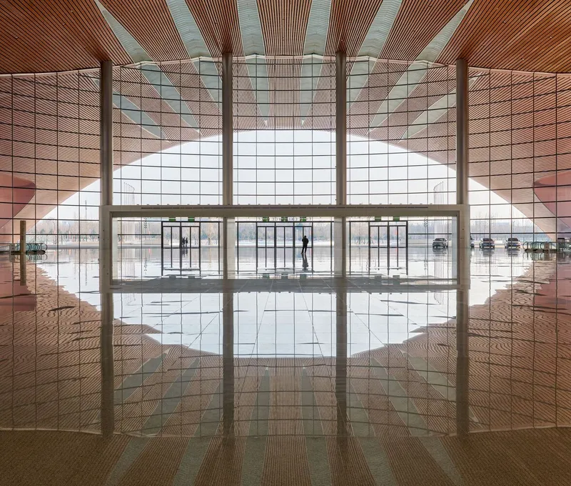 Interior lobby view through perforated metal screens toward the glass entrance with polished floor reflections