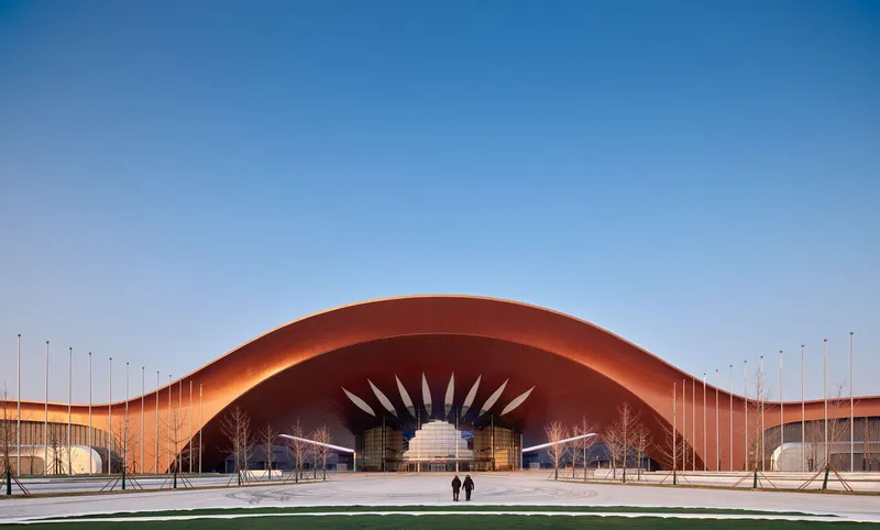 Arched copper-clad roof with radiating blade-like canopy elements and two figures on the plaza at dusk