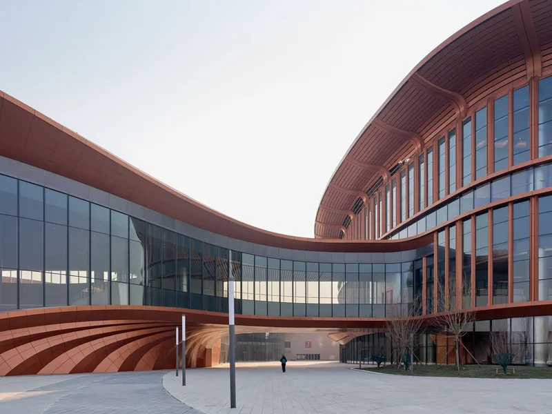 Curved glass facade joining the ribbed copper canopy in the courtyard with a lone visitor walking