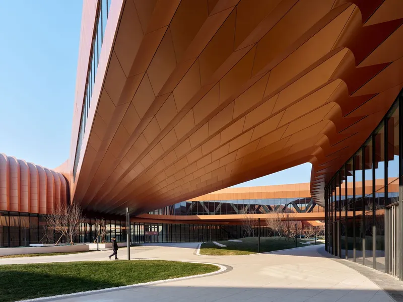 Covered courtyard with ribbed copper-clad soffit curving over a pedestrian pathway on a clear day