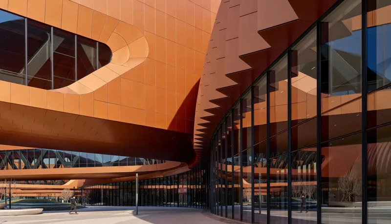 Cantilever with copper panel cladding and serrated edge above glass curtain wall and landscaped courtyard