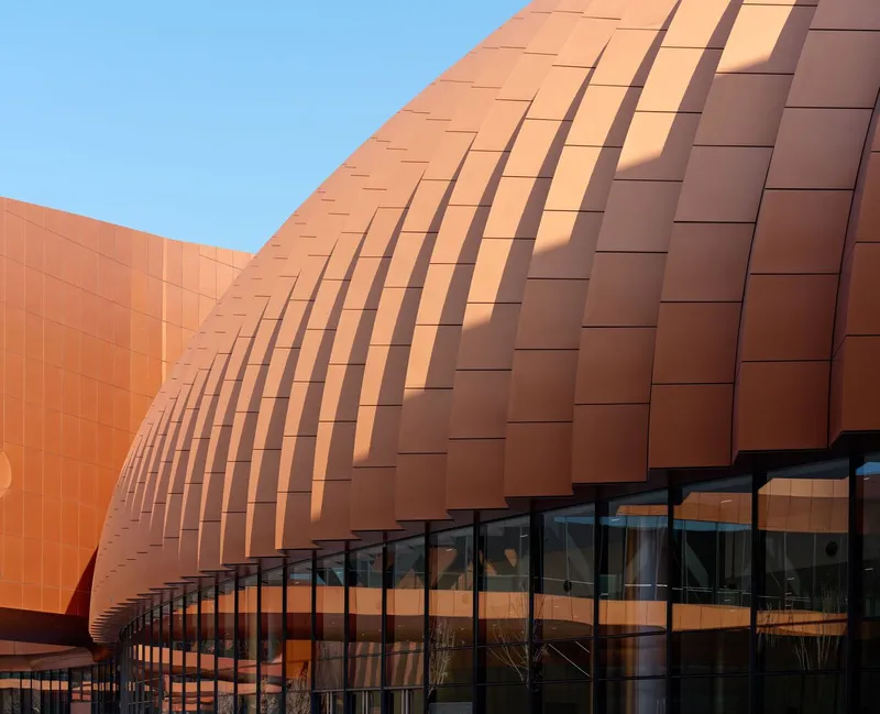 Close-up of copper tile facade with shadow lines creating a rippling pattern in afternoon light
