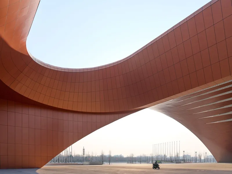 View through a copper-tiled archway opening onto a plaza with a person seated in the distance