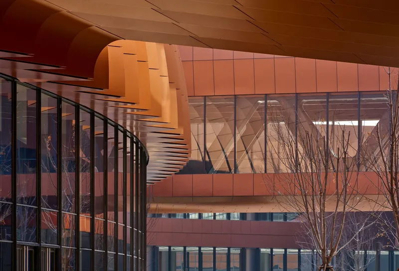 Exterior terrace view showing the curved paneled facade, angular glazing and a bare tree at dusk