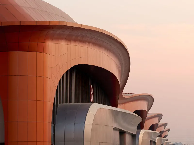 Exterior detail showing curved terracotta-clad volumes with deep arched openings at dusk