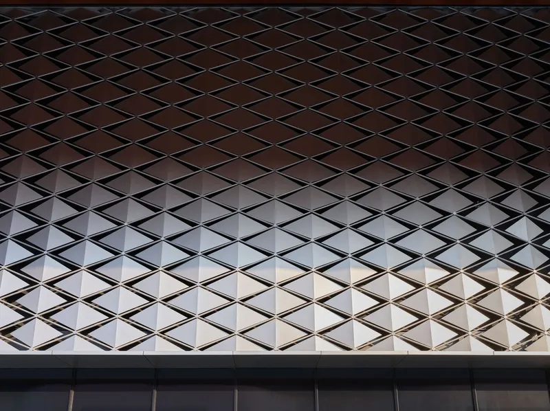 Diamond-patterned metal mesh screen facade transitioning from dark to light across the surface
