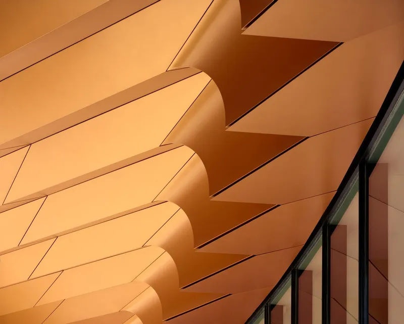 Facade detail of folded terracotta panels creating shadow lines above a row of windows