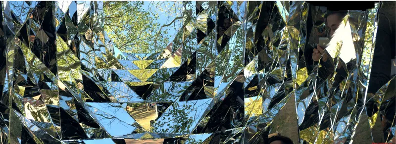 Close-up of angular reflective metal panels capturing fragmented views of sky and foliage