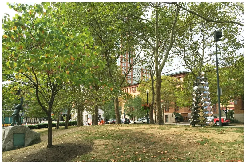 Wide view of the park installation among mature deciduous trees with parked vehicles visible