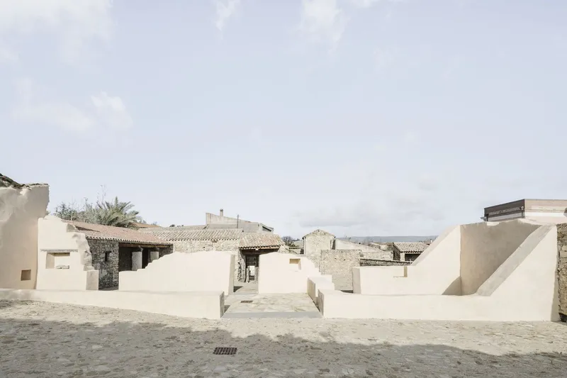 Wide courtyard view with stepped stucco seating platforms facing stone ruins under an overcast sky
