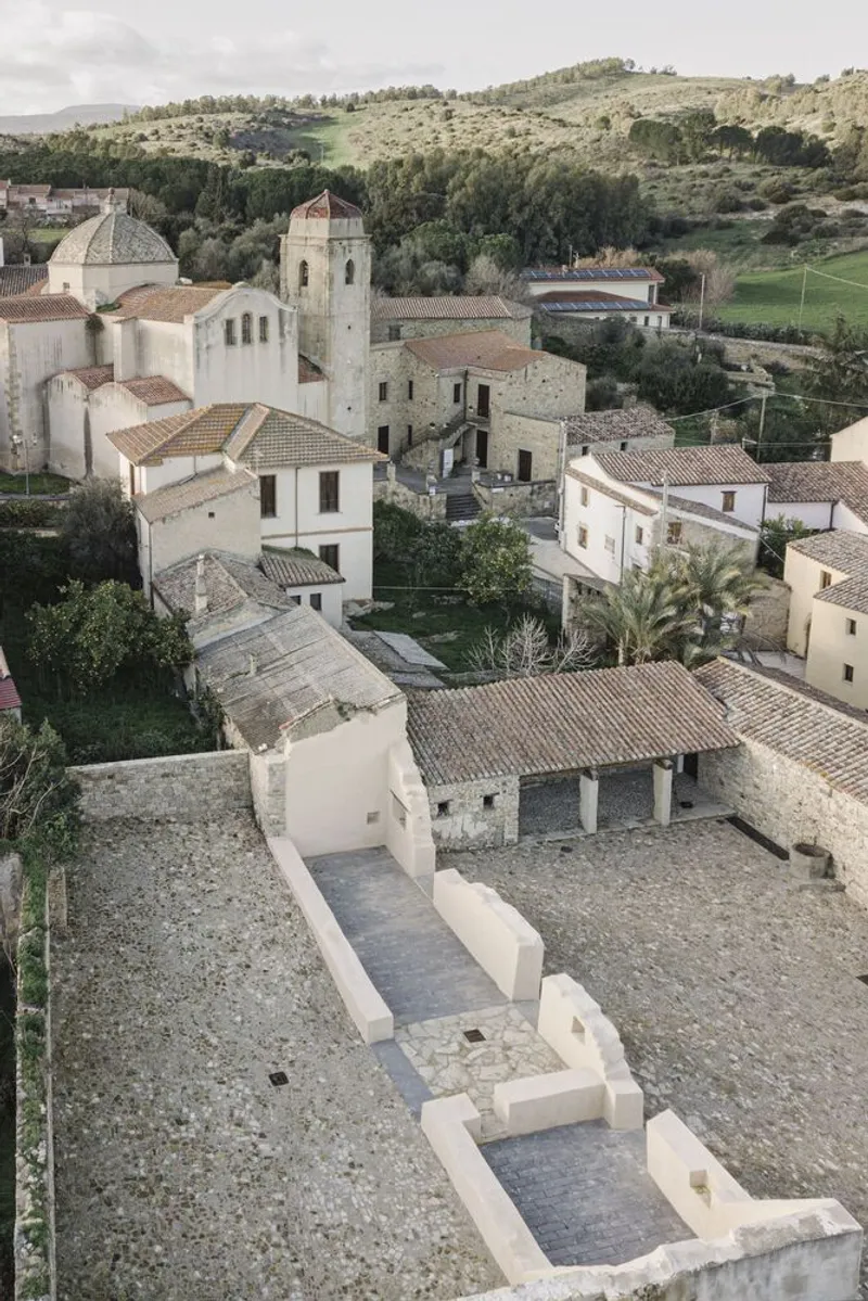 Aerial view of stucco seating platforms in a courtyard surrounded by a hillside village and church tower