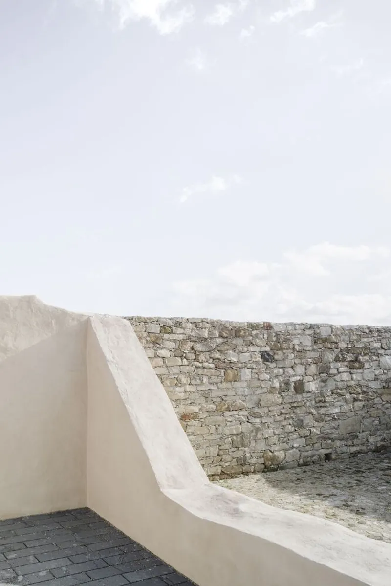 White rendered parapet flowing into an existing stone wall with dark paving below