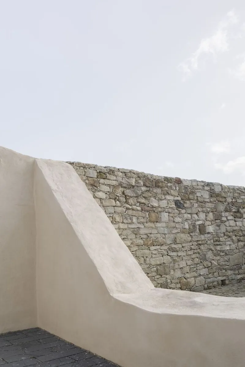 Curved plastered parapet wall transitioning into a historic stone wall under cloudy sky