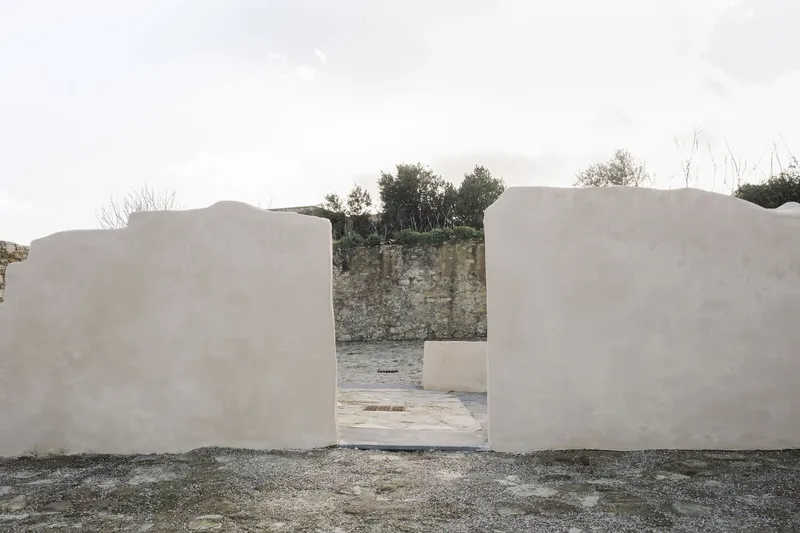 Opening framed by curving white rendered walls revealing stone retaining wall and trees beyond