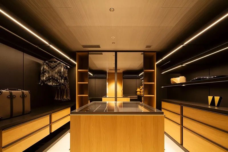 Walk-in closet with central oak island beneath linear cove lighting and dark wood ceiling