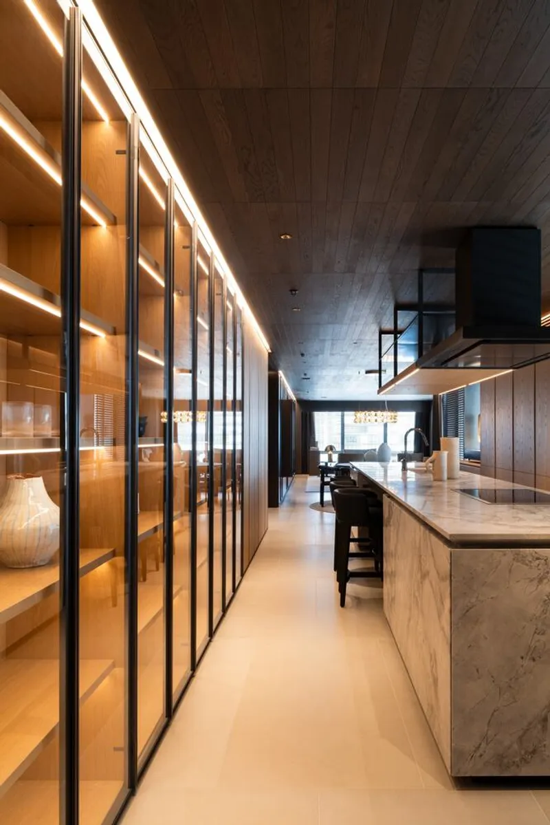 Corridor with floor-to-ceiling glazed display cabinets and marble-clad kitchen island under timber ceiling