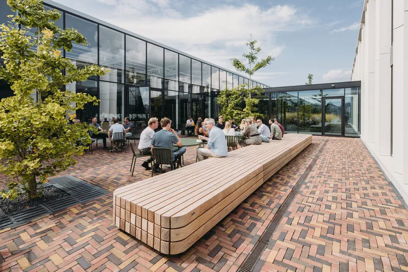 Courtyard terrace with herringbone brick paving, timber benches and people seated among planted trees