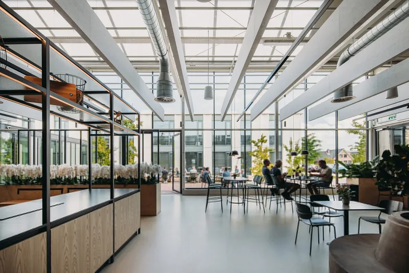 Glazed interior space with exposed white roof trusses, ducting and people at tables