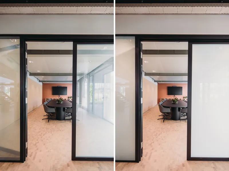 Black-framed glass doors opening to a conference room with exposed concrete ceiling beams