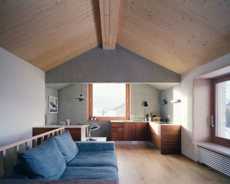 Living space with gabled plywood ceiling and timber window framing a mountain view