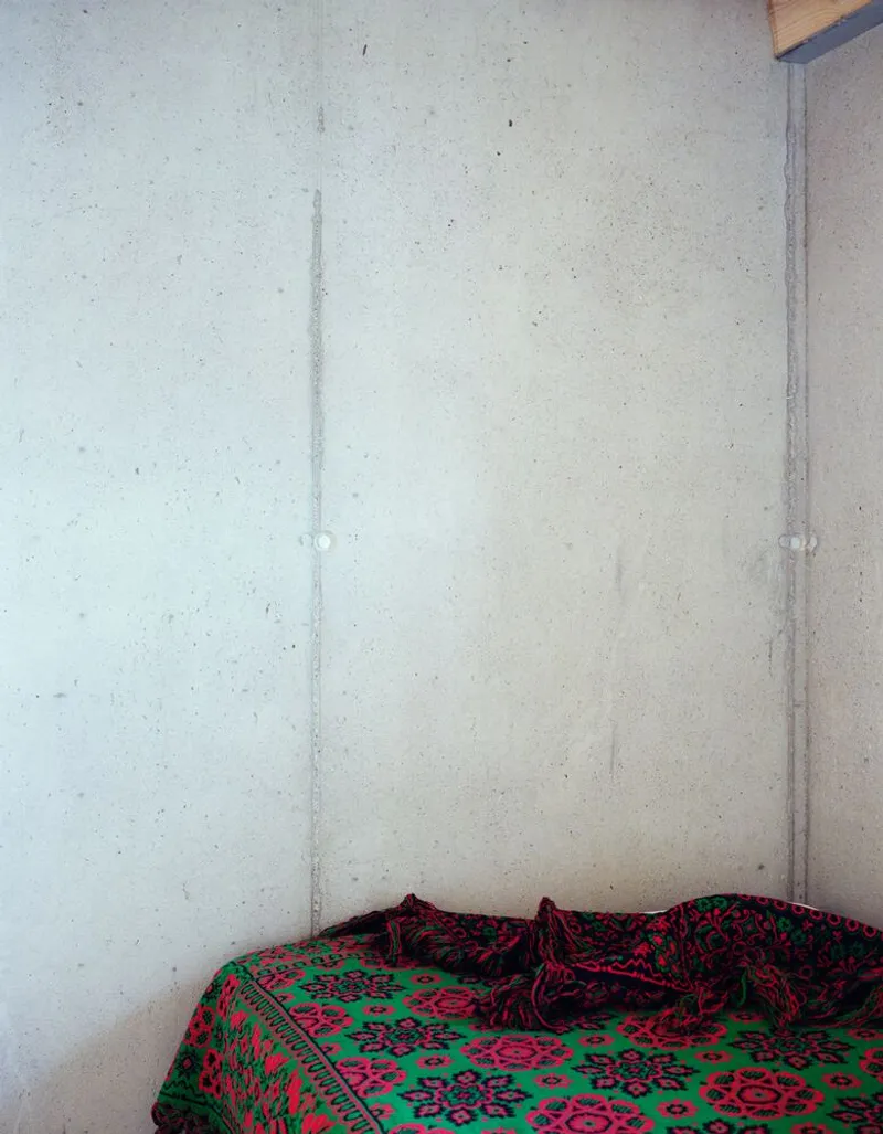 Bedroom corner with concrete walls and patterned textile on a low bed