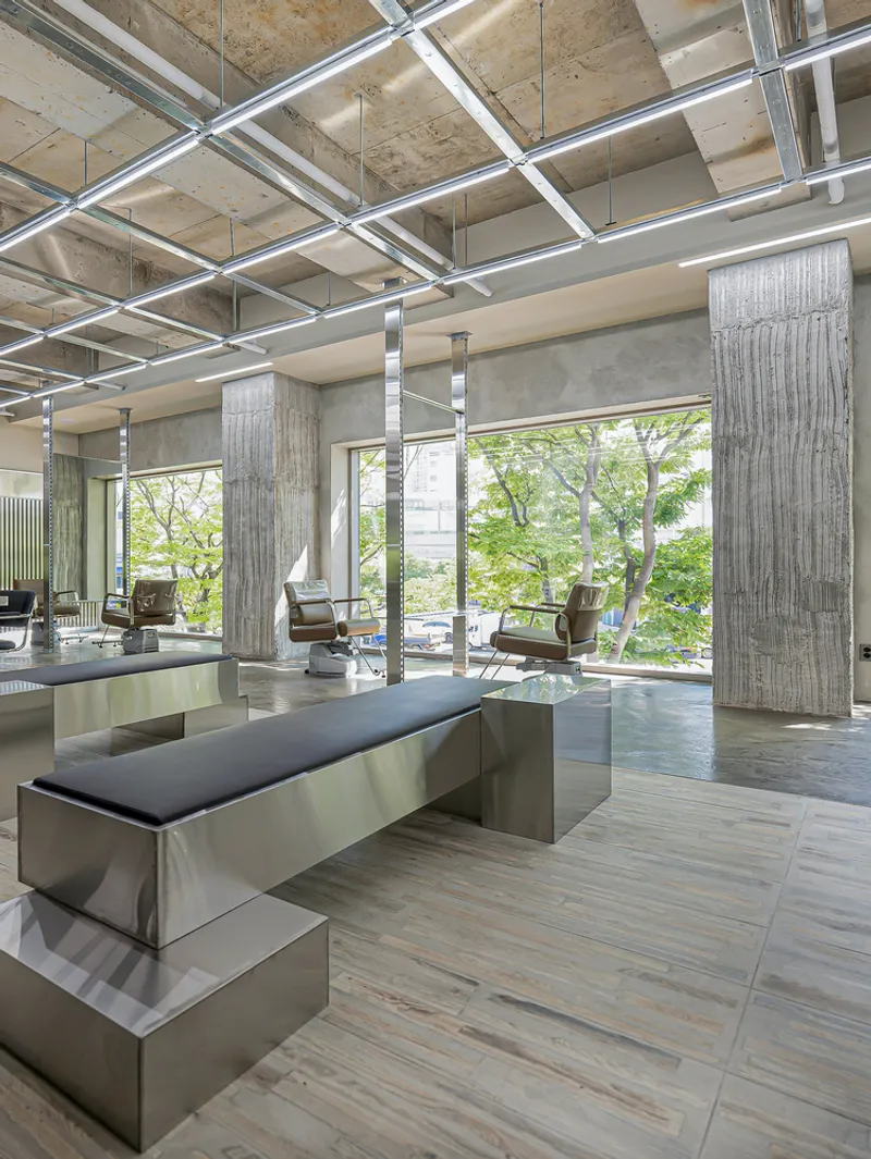 View of stainless steel bench with upholstered cushion beside board-formed concrete columns under an exposed structural ceiling