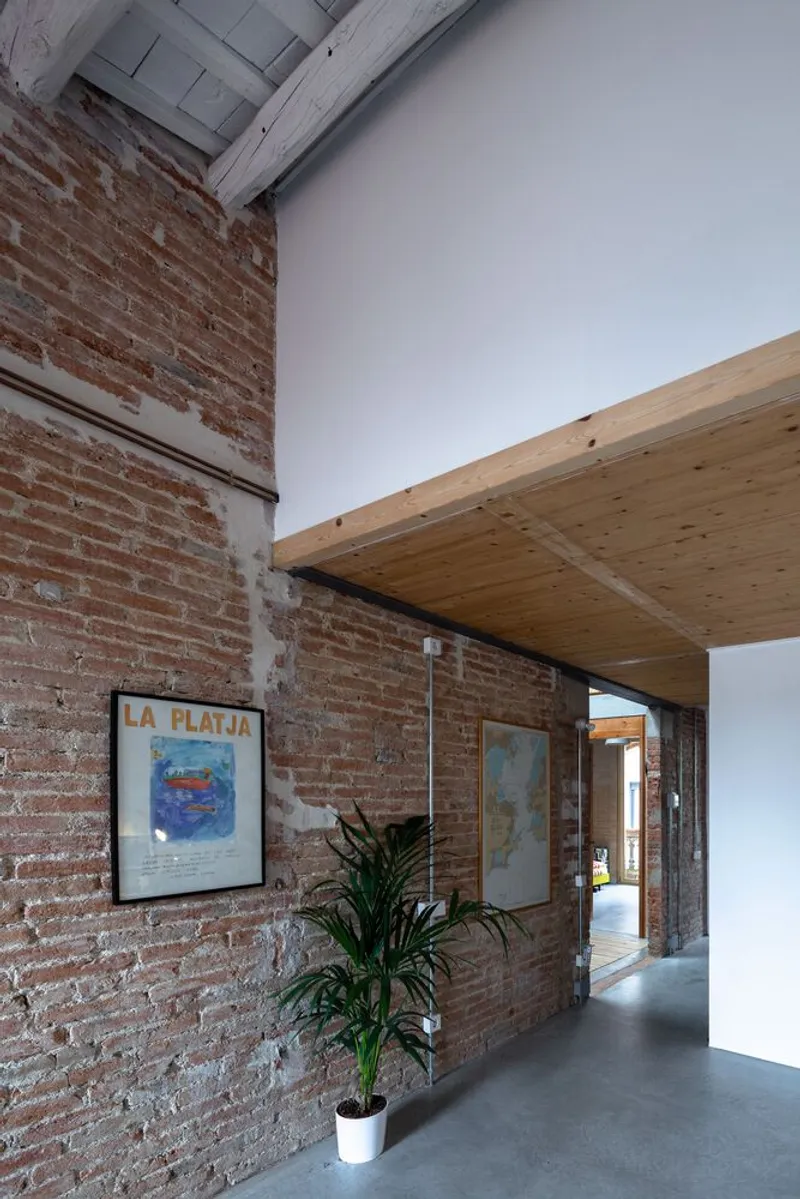Corridor with exposed brick wall, timber ceiling insert, and a framed poster beside a potted plant