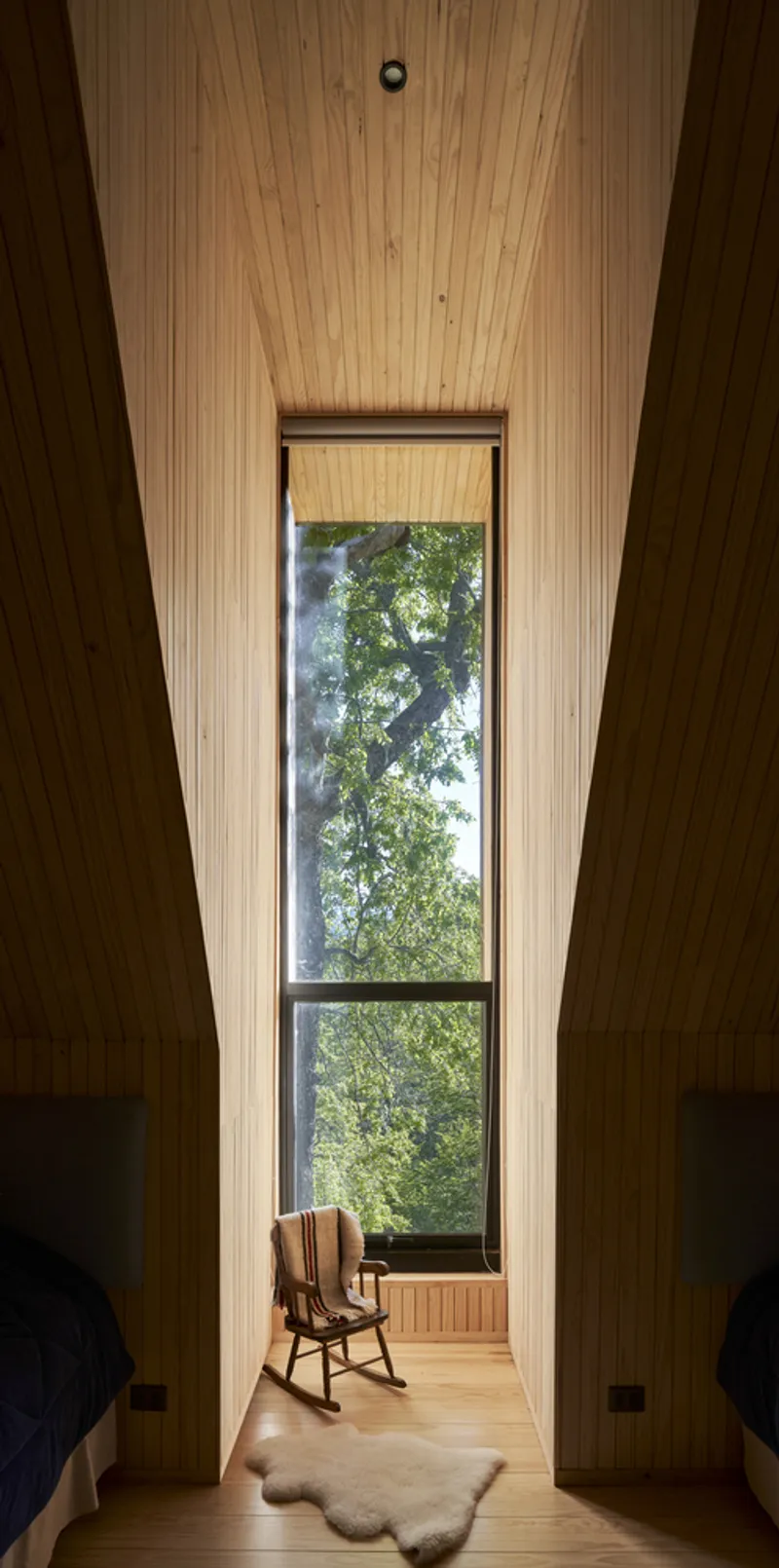 Narrow timber-lined alcove with tall window framing tree views and a rocking chair on the floor