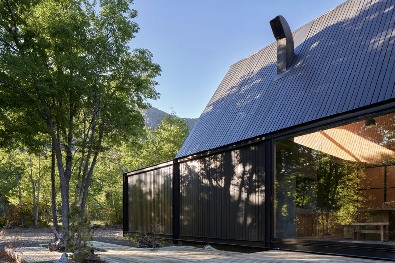 Side elevation showing the sloped metal roof and sliding glass panels under dappled tree shadows