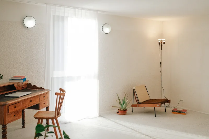 Sparsely furnished white room with sheer curtained doorway and circular wall-mounted lights in soft natural light