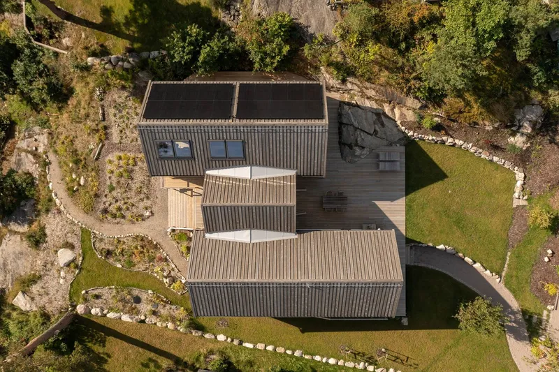 Aerial view of the metal-roofed volumes arranged around a stone-lined garden path and lawn