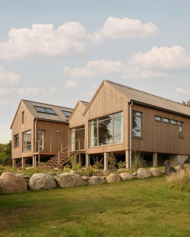Garden facade with timber cladding, elevated entry staircase and large windows under afternoon clouds
