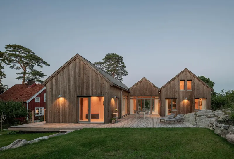View of the illuminated timber-clad volumes with outdoor wall sconces at dusk beside rocky outcroppings