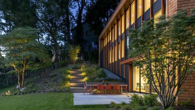 Exterior terrace with dining furniture at dusk, illuminated stairway ascending the landscaped slope beyond