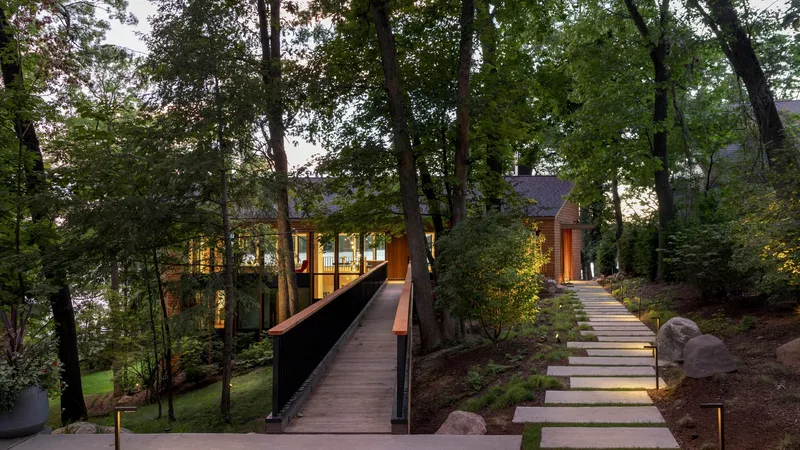 Timber bridge connecting illuminated volumes through the wooded hillside at twilight
