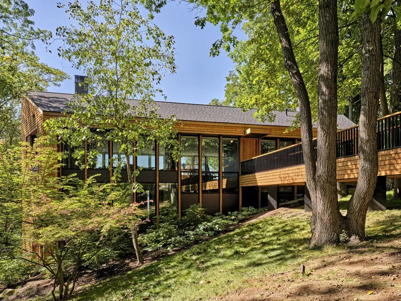 Rear elevation showing cedar cladding and full-height glazing below a deck nestled among mature trees