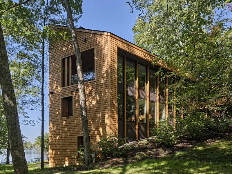 Three-storey cedar-shingled facade with tall glass corner opening facing a wooded hillside