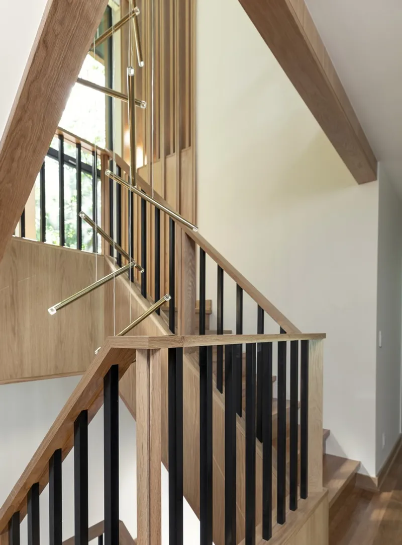 Staircase with timber treads, black metal balusters and exposed wood beam above