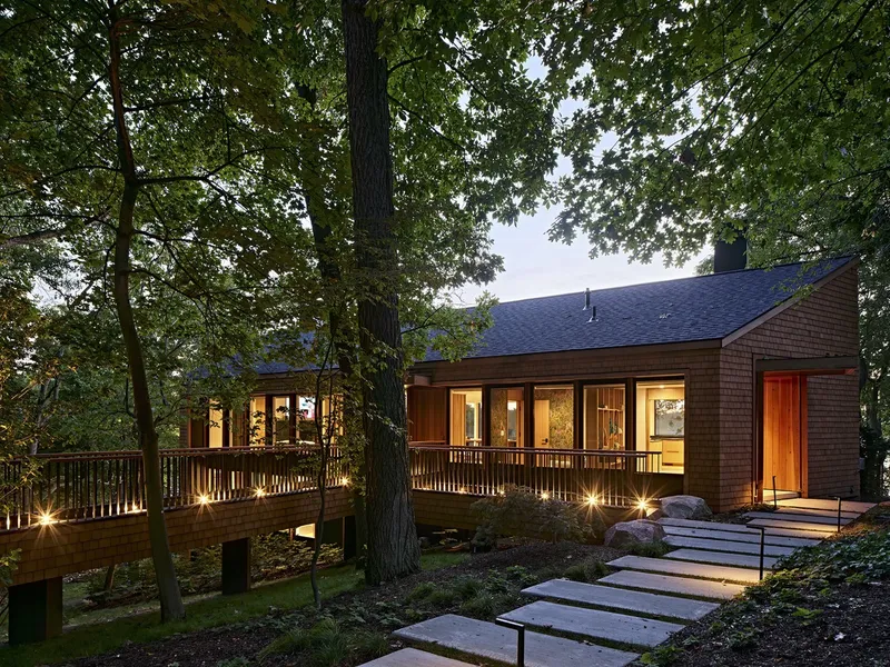 Timber deck with railing connecting to the entrance via stone pavers at dusk
